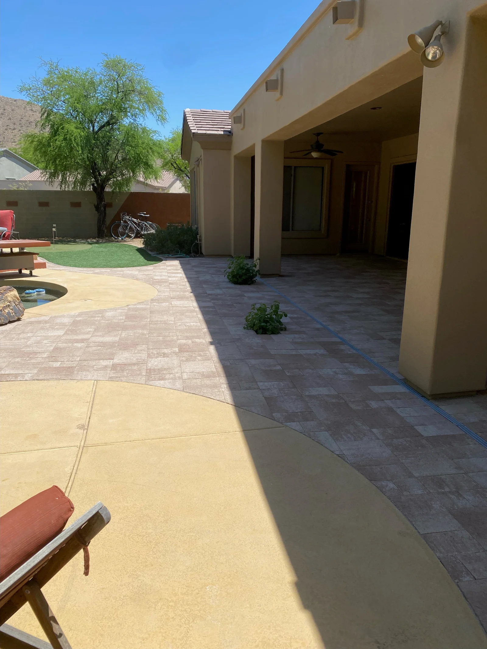 Mixed-tone paver patio with concrete sections, stucco covered structure, and integrated landscaping