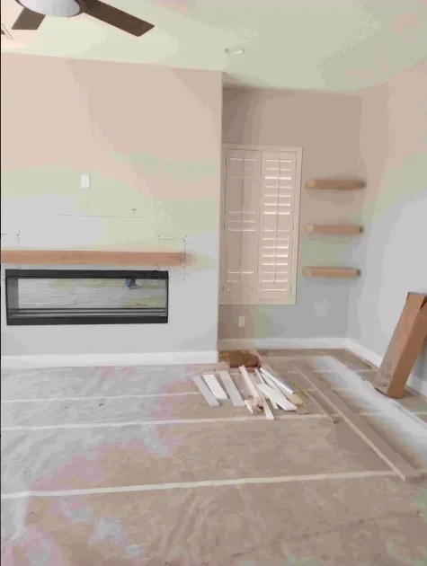 Bedroom renovation in progress with fireplace insert, floating shelves, and drywall finishing